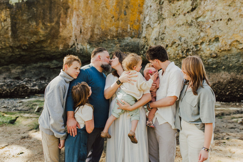 Family of 8 on the beach at Salt Creek near Port Angeles Washington. Family is all snuggled close with mom and dad sharing a kiss.