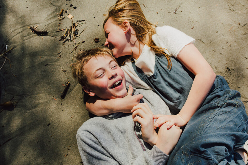 A boy and a girl lying on the beach laughing and smiling