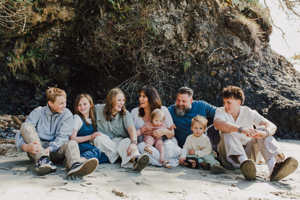 Family of 8 sitting on the beach at Salt Creek together smiling and laughing.