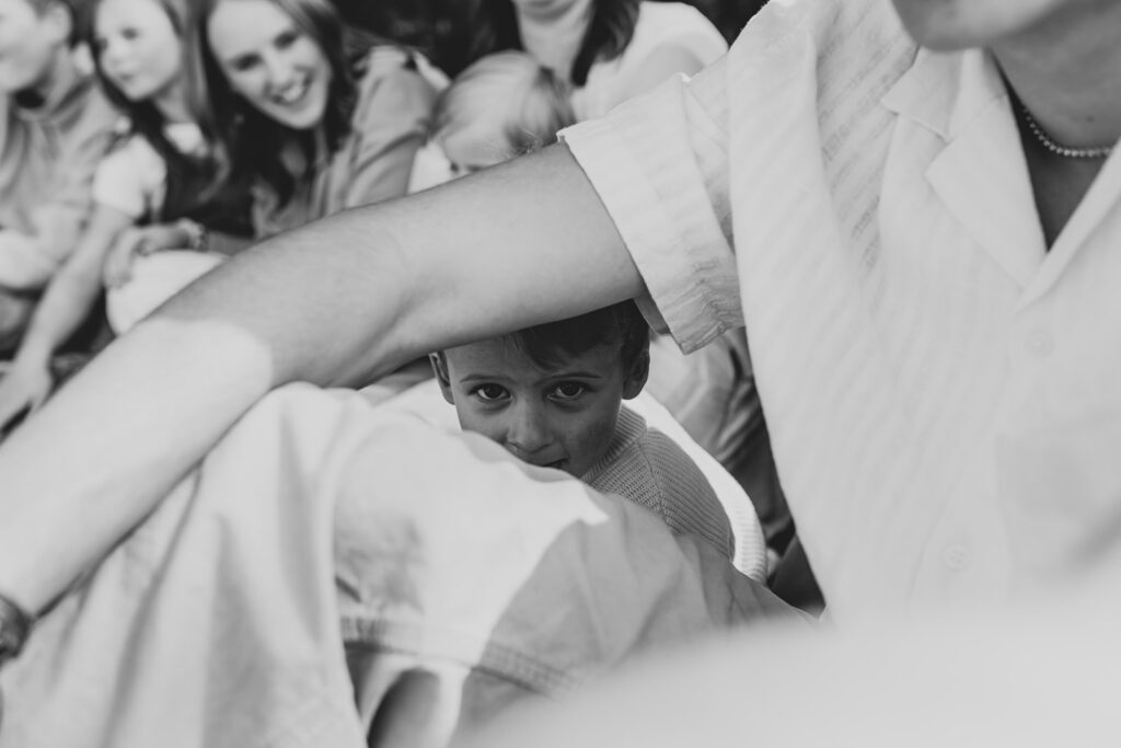 Black and white image of a toddler boy peeking around his brother's arm