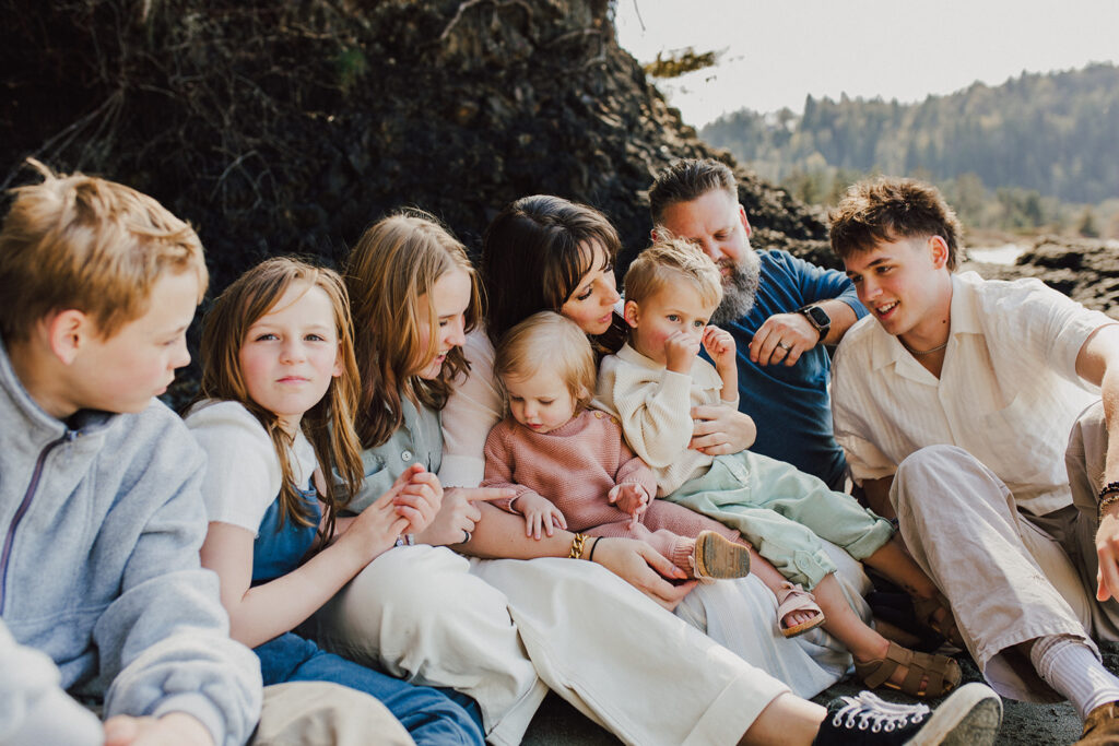 Family sitting together on the beach. They are color coordinated in blues, creams, pink and green. 