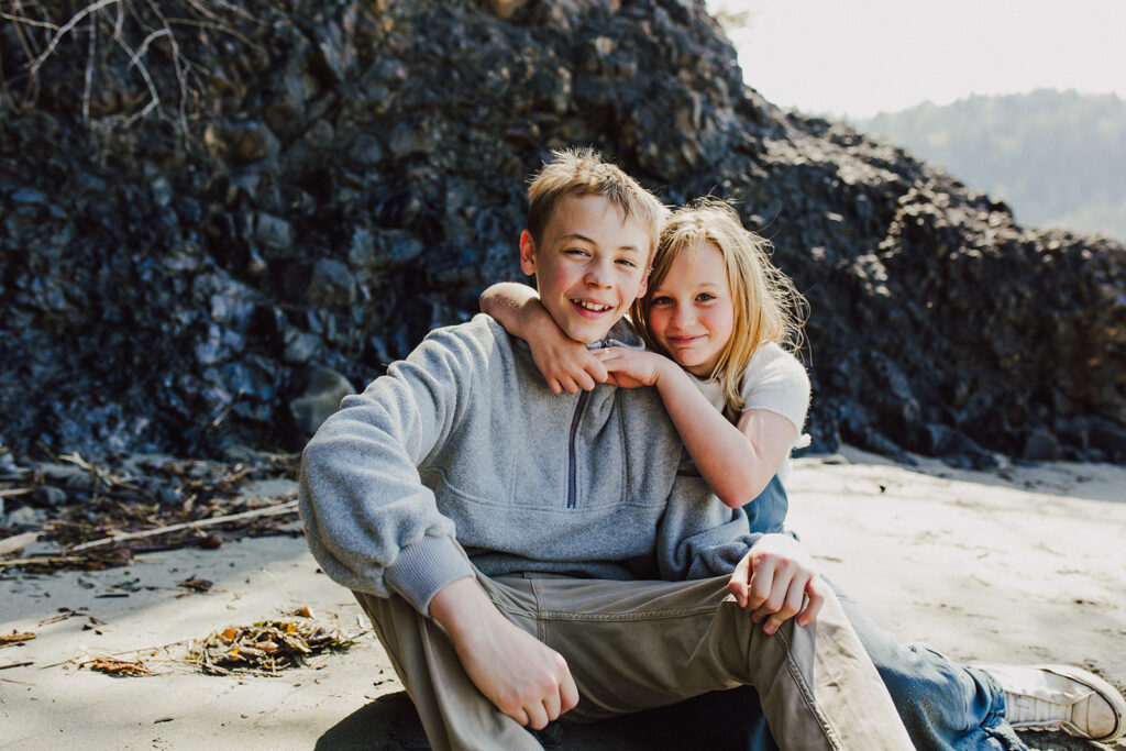 Image of 2 children, a boy and a girl sitting on the beach at Salt Creek with a black rock wall behind them. 