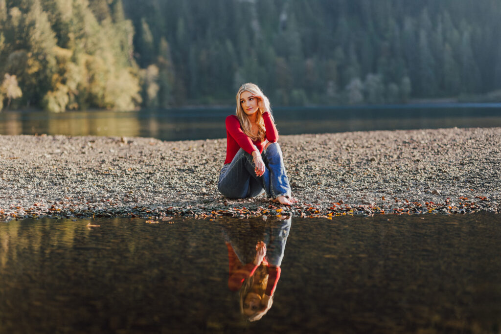 A girl sits by Lake Crescent with trees and a bright sun.