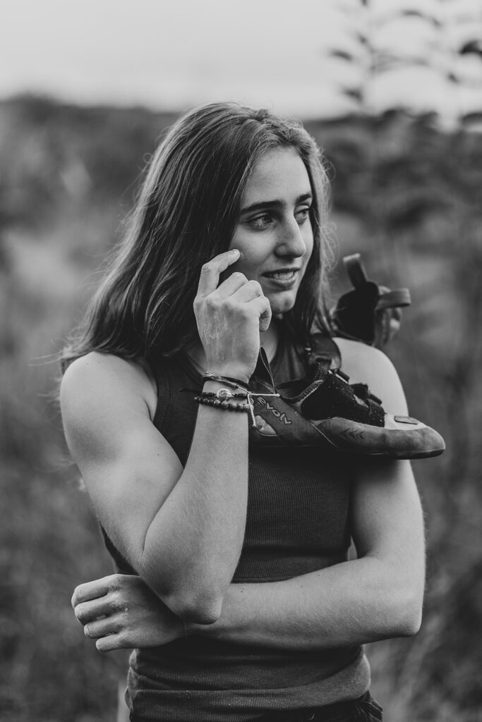A girl holding her rock climbing shoes with chalk on her hands
