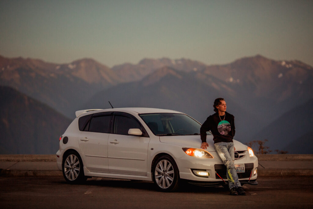 A young man leaning on the hood of his car at Hurricane Ridge at sunset