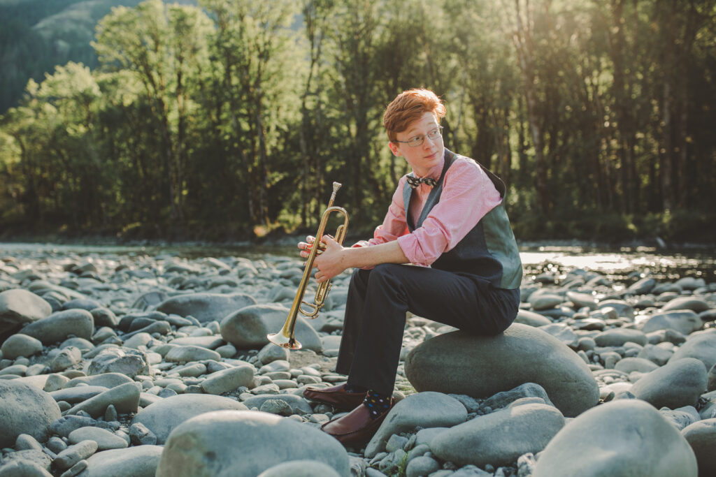 A young man seated by a river holding a trumpet