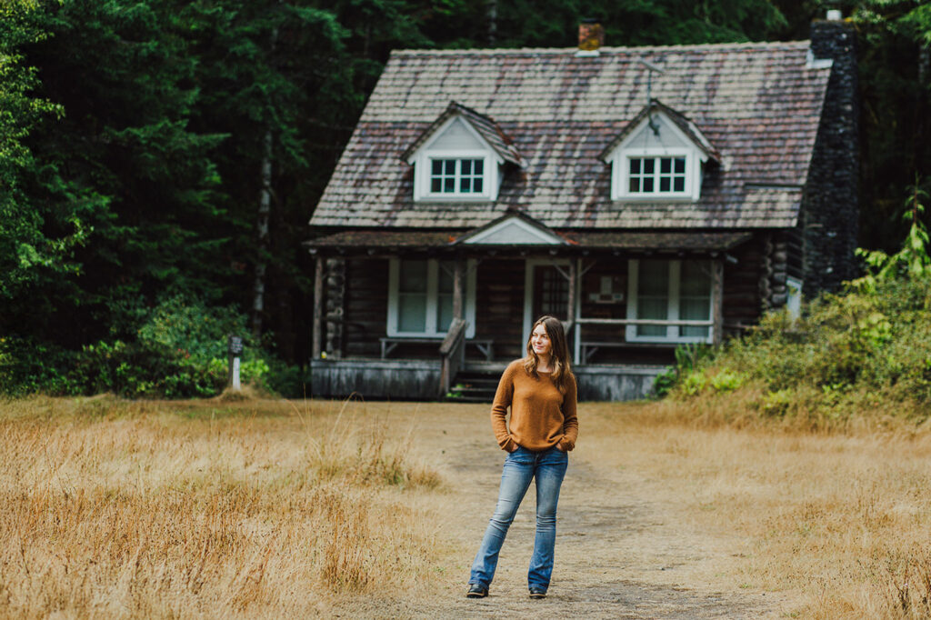 A teenage girl standing on a path with a cabin behind her