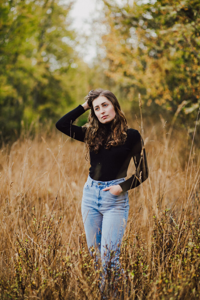 A teen age girl stands in a field with tall brown grass