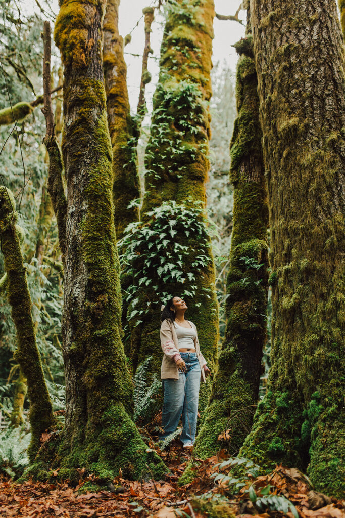 Teenage girl standing in the forest looking up at trees