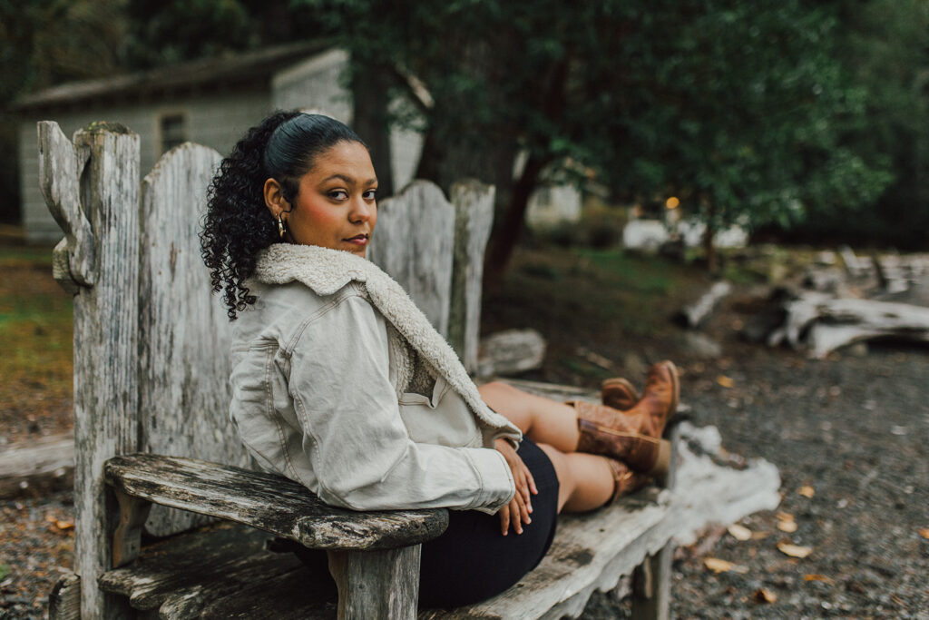 Girl sitting on rustic bench wearing jacket dress and cowboy boots