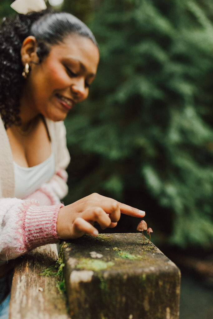 Girl looking at two tiny mushrooms growing on a wooden post