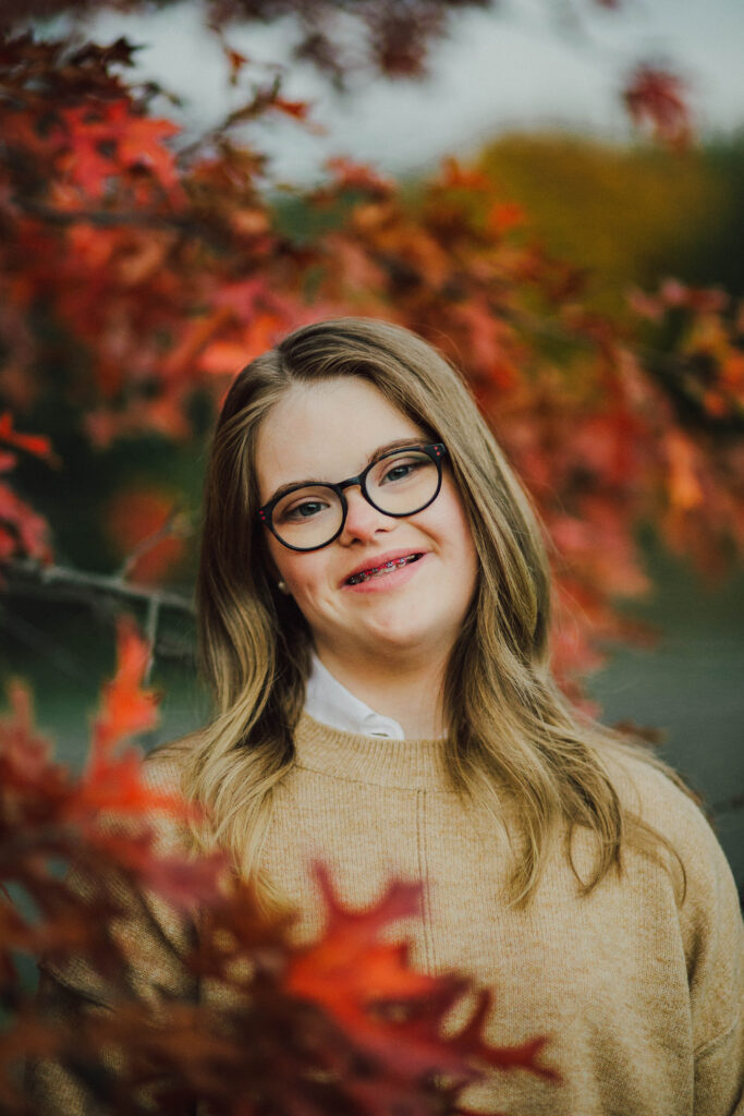 A teenage girl standing next to a tree in the fall with changing leaves